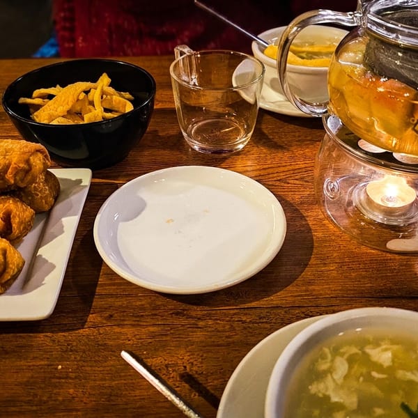 Wooden restaurant table with three fried rolls, chips, soup, tea in a glass teapot, and empty plates.