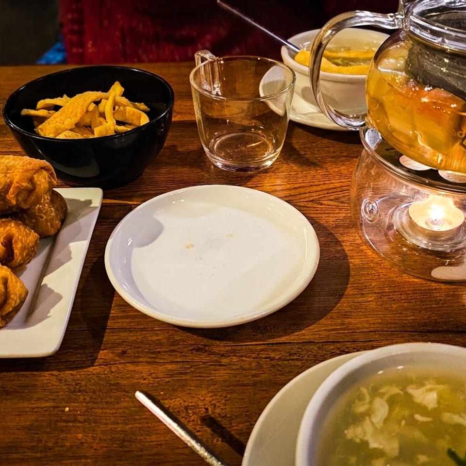 Wooden restaurant table with three fried rolls, chips, soup, tea in a glass teapot, and empty plates.