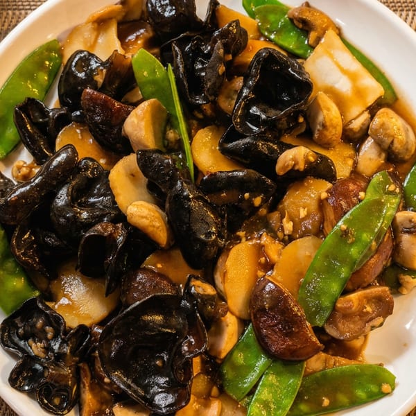 Plate of stir-fried mushrooms, black fungus, snow peas, and vegetables in savory sauce.