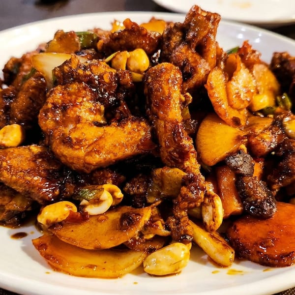 Plate of glazed stir-fried meat, vegetables, mushrooms, and peanuts served on a white dish at a restaurant table.