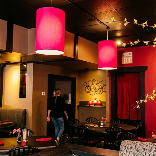 Warmly lit restaurant dining room with red pendant lights, black tables, booth seating, red accents, and decorative flowering branches.