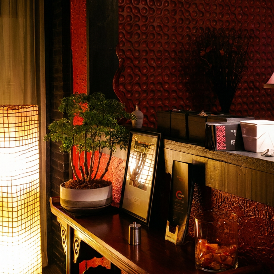 Warmly lit restaurant interior with glowing shoji screens, red textured walls, decorative lamps, framed menus, and a potted plant.