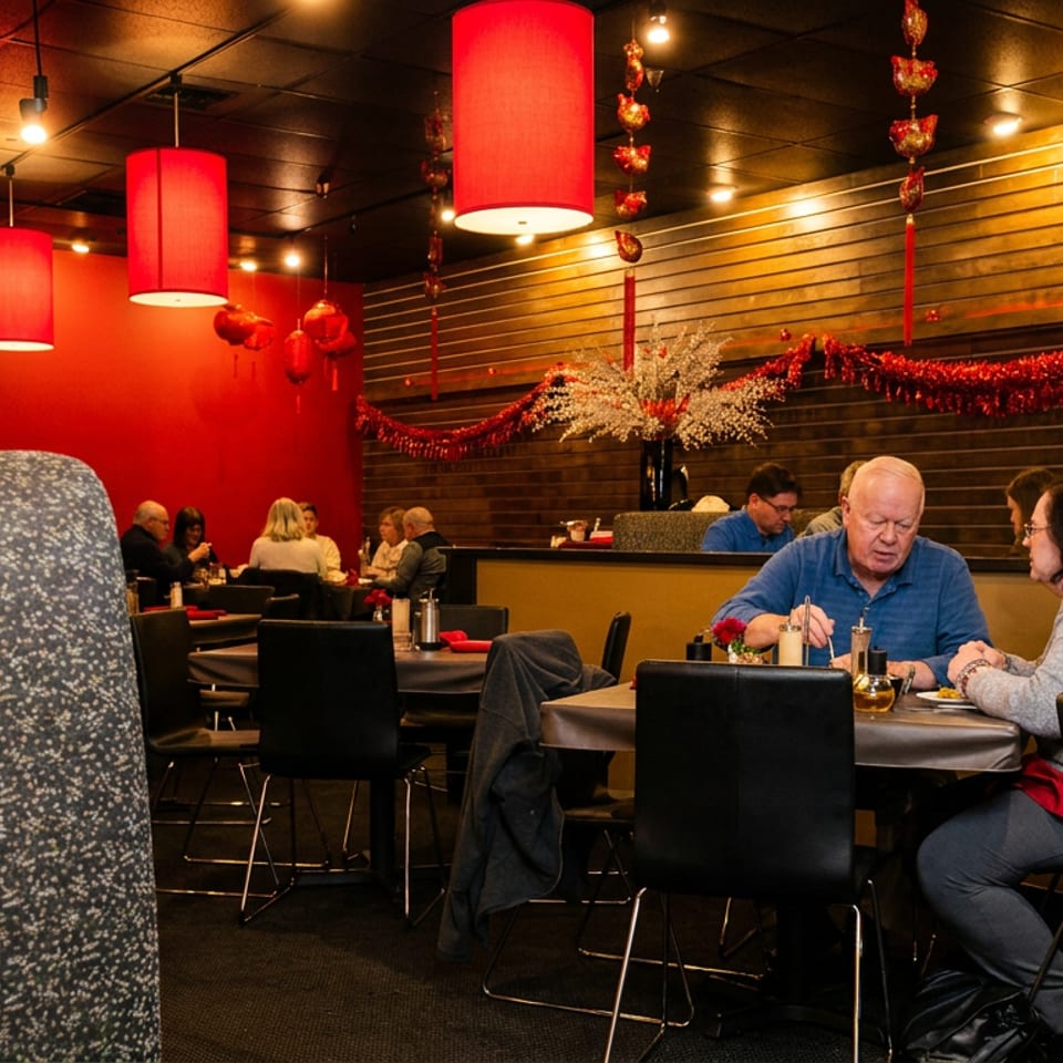 Warmly lit restaurant dining room with red pendant lights, festive decorations, wood-paneled walls, and seated diners.