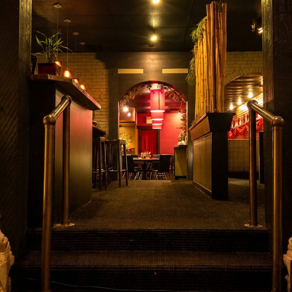 Warmly lit Asian restaurant entrance with red walls, black steps, bamboo decor, and guardian lion statues flanking the staircase.