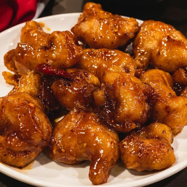 Plate of golden-brown fried chicken pieces coated in glossy sauce, served on a restaurant table with a red napkin.